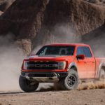 A red 2021 Ford F-150 Raptor is shown off-roading during a 2021 Ford F-150 vs 2021 Chevy Silverado comparison.