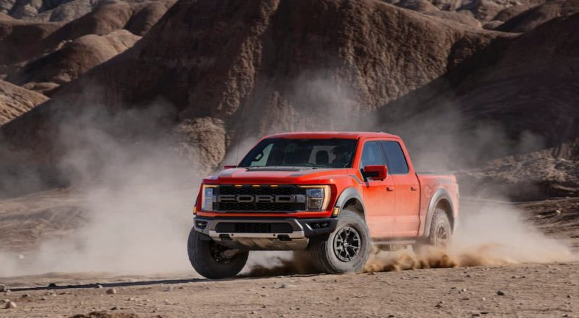 A red 2021 Ford F-150 Raptor is shown off-roading during a 2021 Ford F-150 vs 2021 Chevy Silverado comparison.