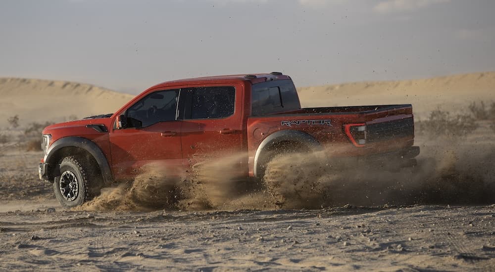 A red 2022 Ford F-150 Raptor is shown from the side while drifting in dirt.