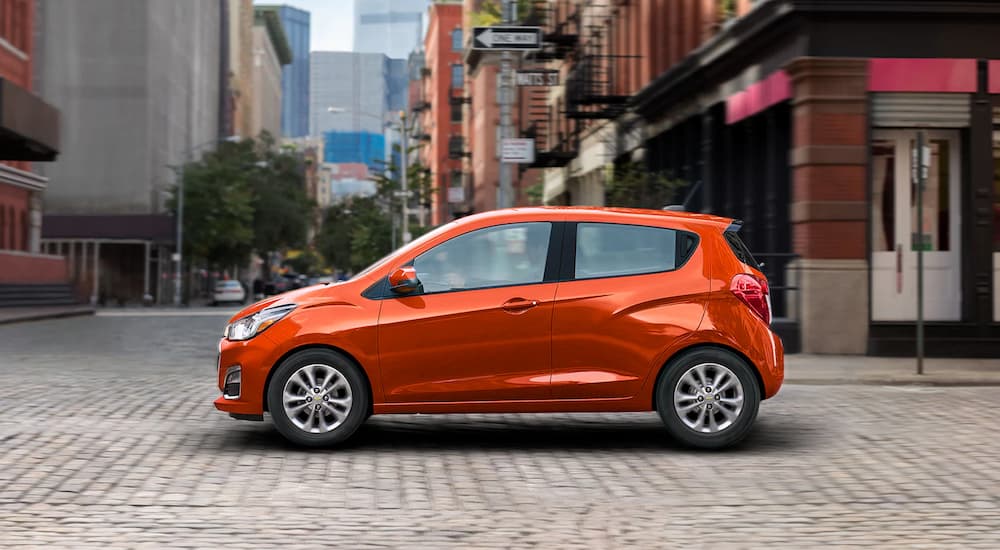 An orange 2022 Chevy Spark is shown from the side driving on a city street.