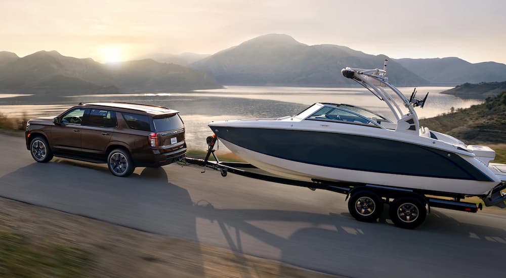 A brown 2022 Chevy Tahoe RST is shown towing a boat near a body of water.