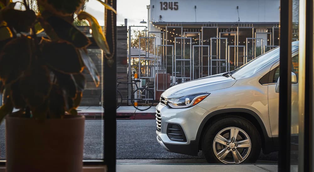 The front half of a silver 2022 Chevy Trax is shown parked outside of a storefront.