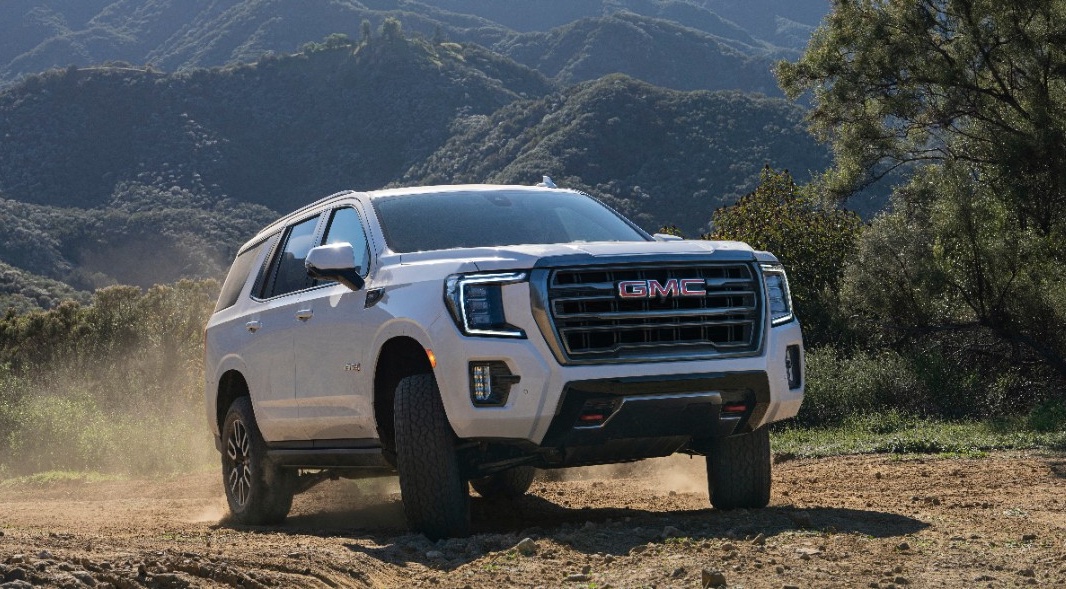 A white 2022 GMC Yukon AT4 is shown driving on a dusty trail.