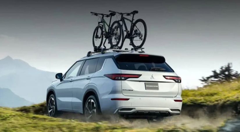 A white 2022 Mitsubishi Outlander is shown from the rear with bikes loaded on top after leaving a Mitsubishi dealer near you.