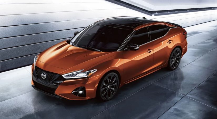 An orange 2022 Nissan Maxima is shown driving through a garage.
