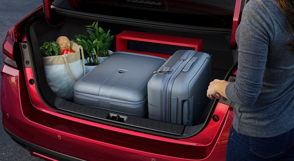 A woman is shown putting luggage and supplies into the trunk of a red 2022 Nissan Versa.
