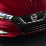A close up of the front of a red 2022 Nissan Versa is shown while driving.