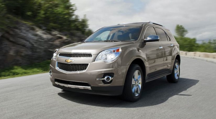 A tan 2013 Chevy Equinox LTZ is shown driving on a empty road.