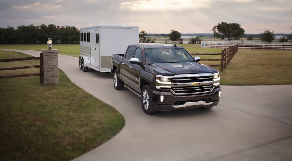A black 2017 Chevy Silverado 1500 High Country is shown towing a horse trailer on a farm.