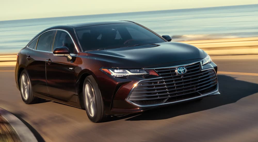 A maroon 2020 Toyota Avalon is shown driving past a body of water.