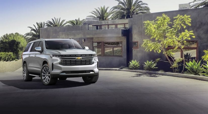 A silver 2022 Chevy Suburban is shown in front of a modern house.