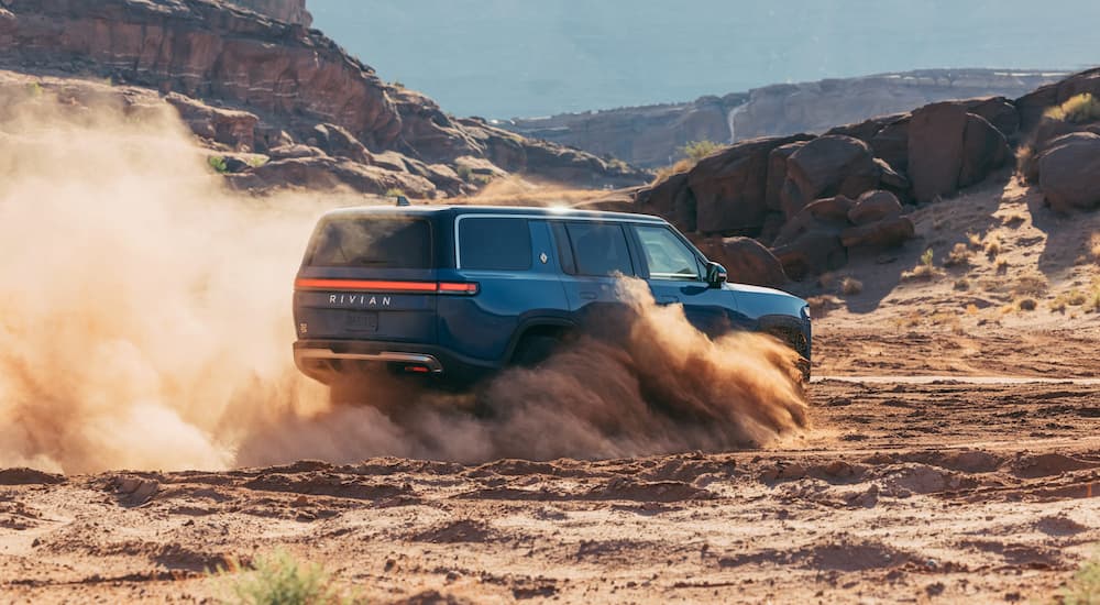 A blue 2022 Rivian R1S is shown kick up dust in the desert.