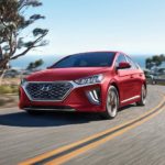 A red 2022 Hyundai IONIQ Hybrid is shown driving with a distant ocean.