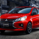 A red 2022 Mitsubishi Mirage is shown driving through a city at night.