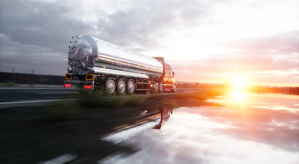 A fuel tanker is shown driving on a highway at dusk.