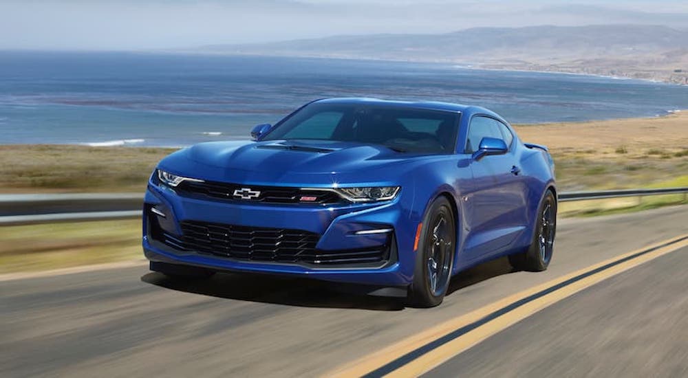 A blue 2020 Chevy Camaro SS is shown driving on a highway past a body of water.