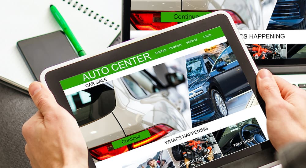 A person is shown holding a tablet while looking at an online car dealer.