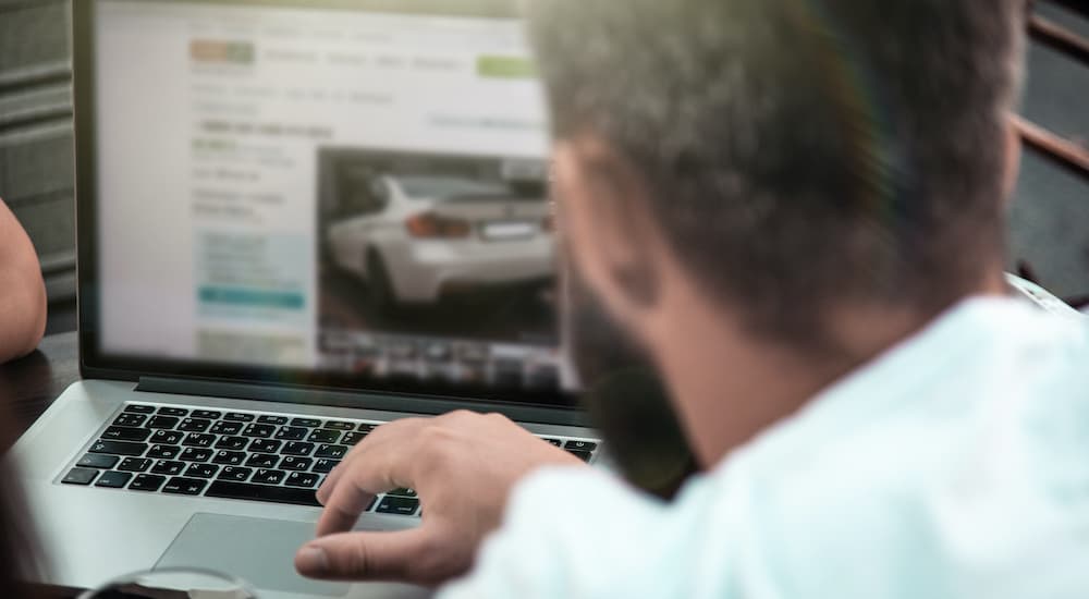 A man is shown using a laptop to look at an online car dealer.