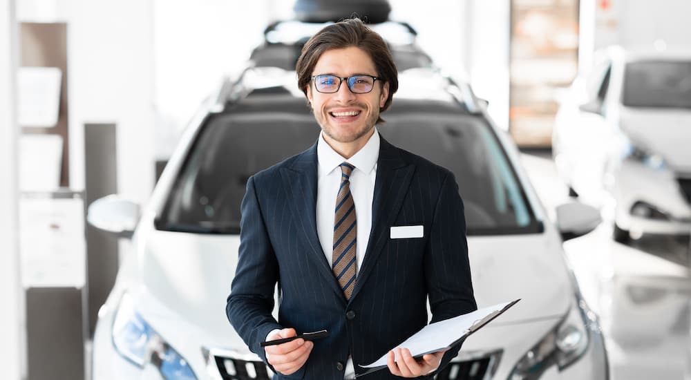 A salesman is shown holding paperwork while standing in front of a vehicle after searching 'auto loans near you'.