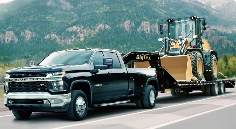 A black 2020 Chevy Silverado 3500 is shown from the front at an angle while it tows a trailer loaded with a loader.