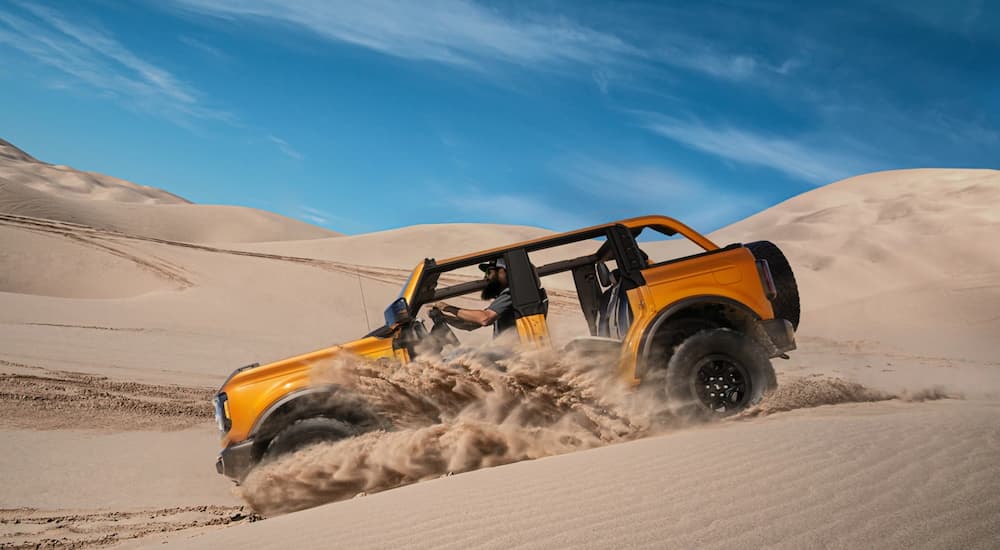 A gold 2021 Ford Bronco Wildtrak Sasquatch is shown from the side off-roading in the desert.