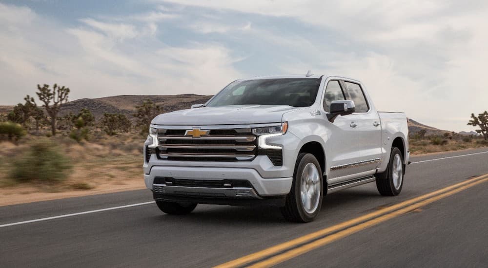 A white 2022 Chevy Silverado High Country is shown from the front at an angle on a desert road.