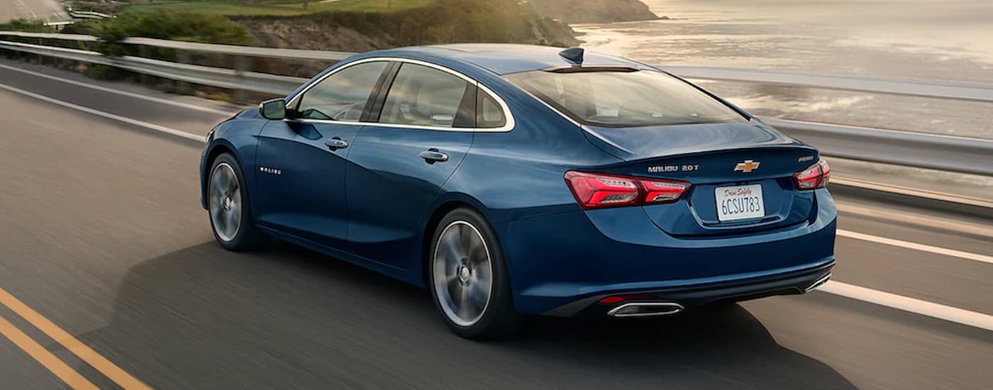 A blue 2022 Chevy Malibu is shown from the rear driving on an open highway.