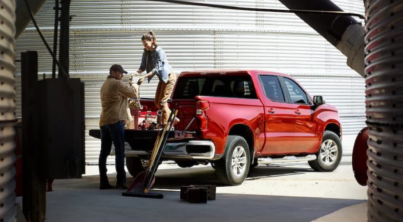 Two people are shown loading supplies into the bed of a red 2022 Chevy Silverado Limited.