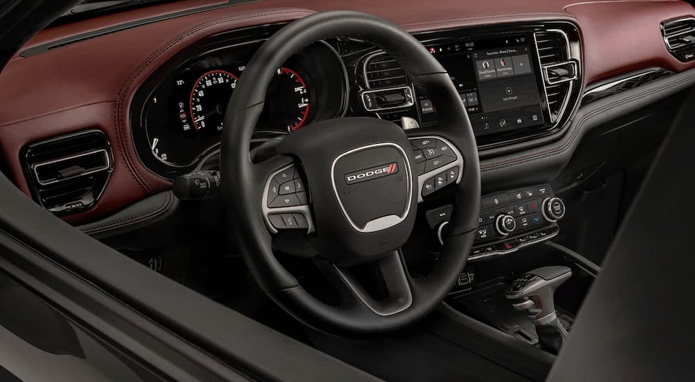 The black and red interior of a 2022 Dodge Durango SRT shows the steering wheel and dashboard.