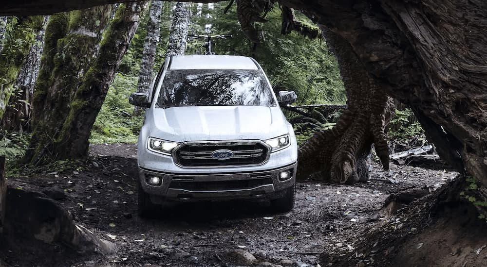 A white 2022 Ford Ranger Lariat is shown from the front driving on a forest trail.
