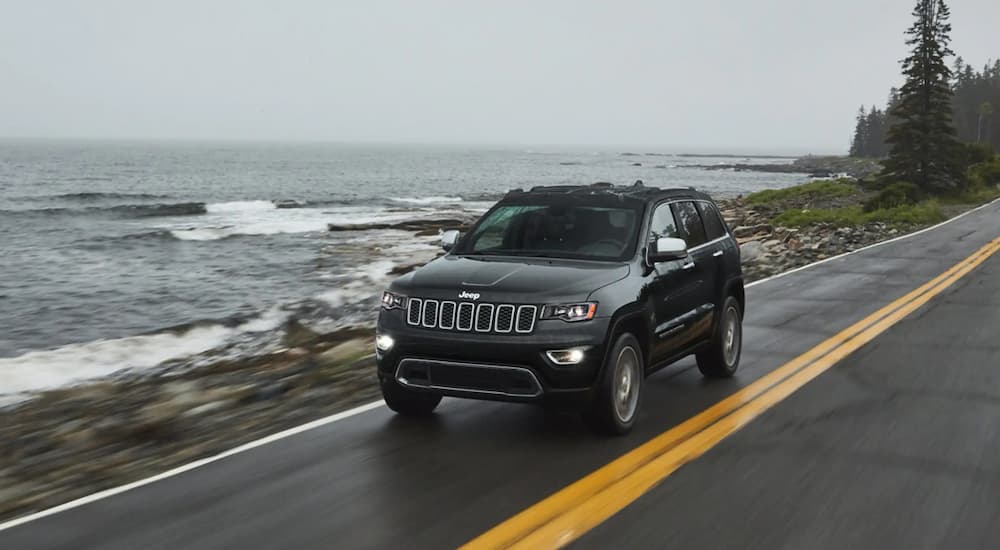 A black 2022 Jeep Grand Cherokee WK is shown driving on a road next to the ocean.