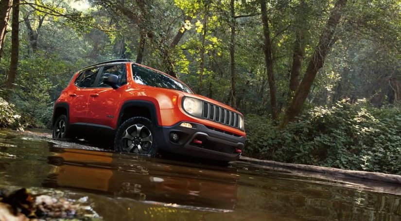 An orange 2022 Jeep Renegade is shown driving through a deep muddy puddle.