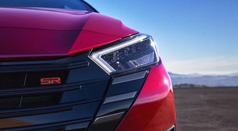A close up shows the driver side headlight on a red 2022 Nissan Versa SR.