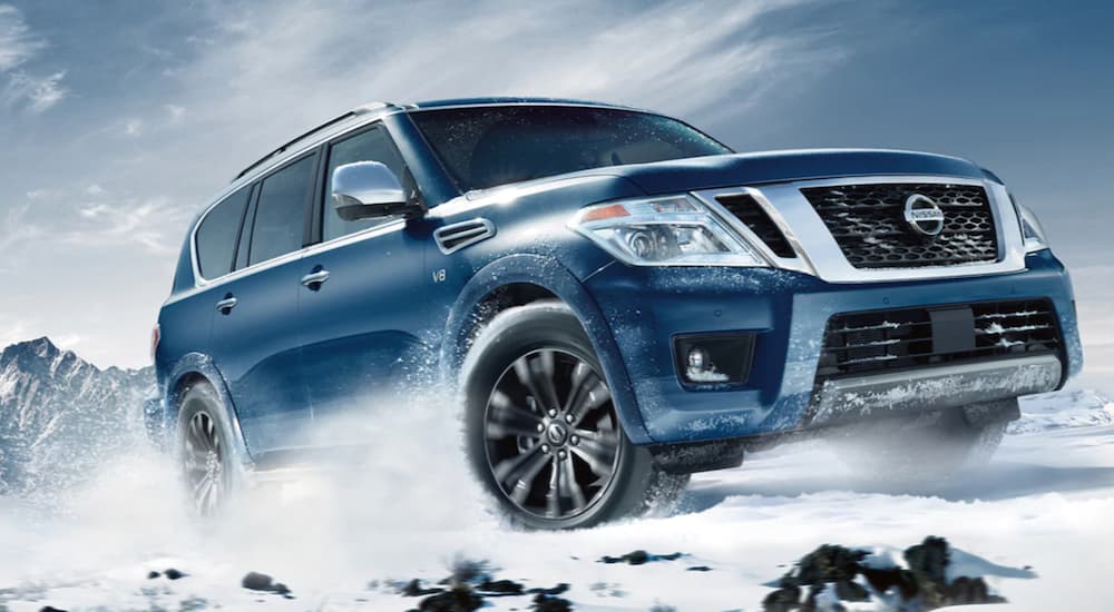 A blue 2020 Nissan Armada is shown from the front at an angle while driving through snowy mountains.
