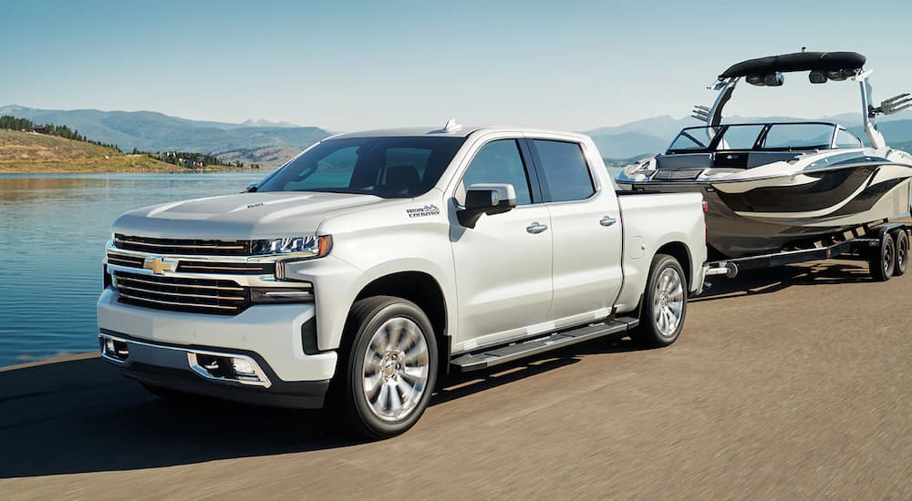 A white 2022 Chevy Silverado 1500 High Country is shown towing a boat past a body of water.