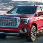 A red 2022 GMC Yukon Denali is shown from the front driving through a snowy area during a 2022 GMC Yukon vs 2022 Toyota Sequoia comparison.