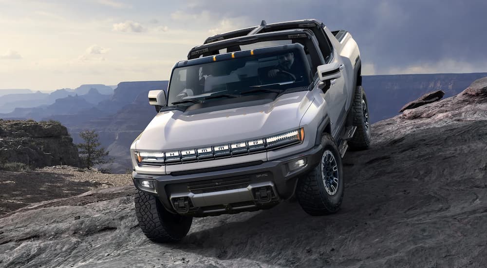 A silver 2022 GMC Hummer EV Pickup is shown driving off-road over rocks.