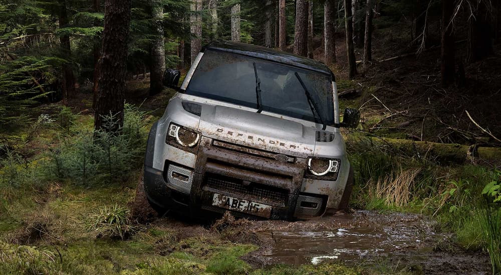A silver 2023 Land Rover Defender 90 is shown driving through a large mud puddle.