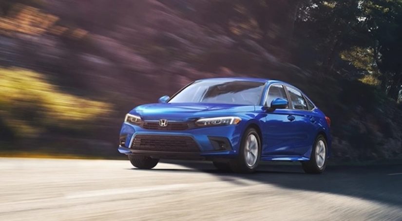A blue 2022 Honda Civic is shown driving from the front at an angle after leaving a Honda dealer near you.