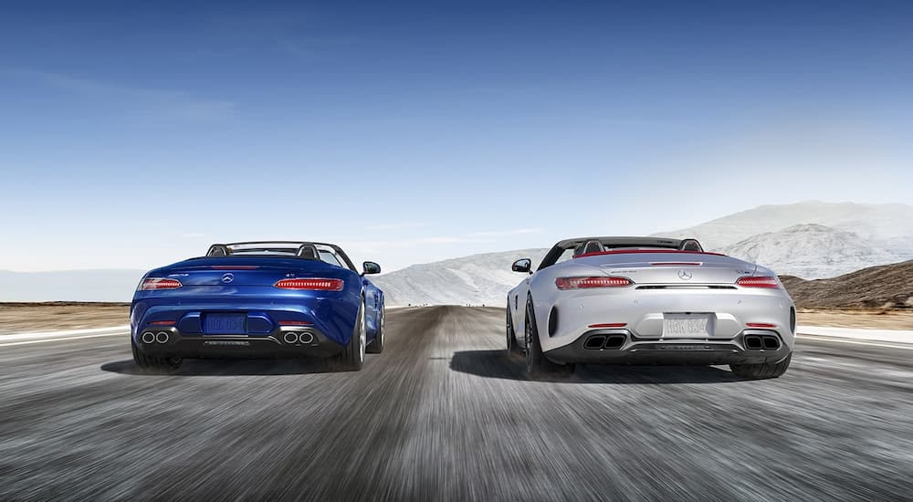 A blue and a silver 2021 Mercedes AMG GT Roadster are shown from the rear driving side-by-side.