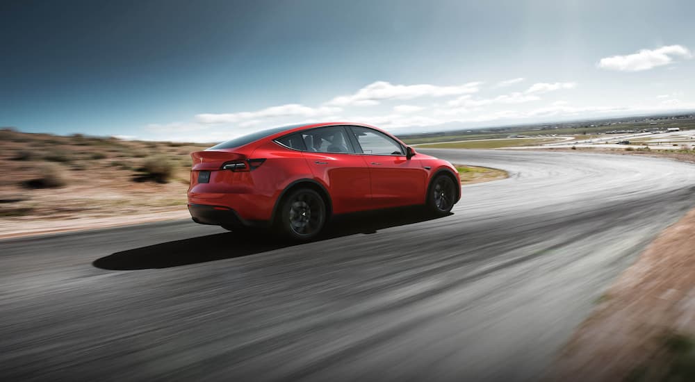 A red Tesla Model Y is shown from a rear angle driving on an open highway.