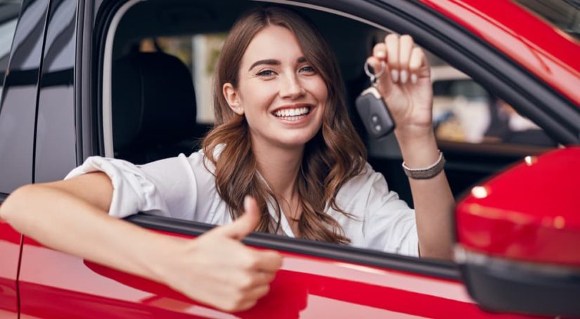 A woman is shown holding a car key while sitting in a red vehicle.