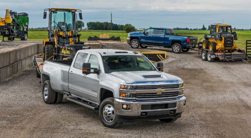 A sliver 2018 Chevy Silverado 3500 is shown from the front at an angle hooked up to a trailer at a job site.