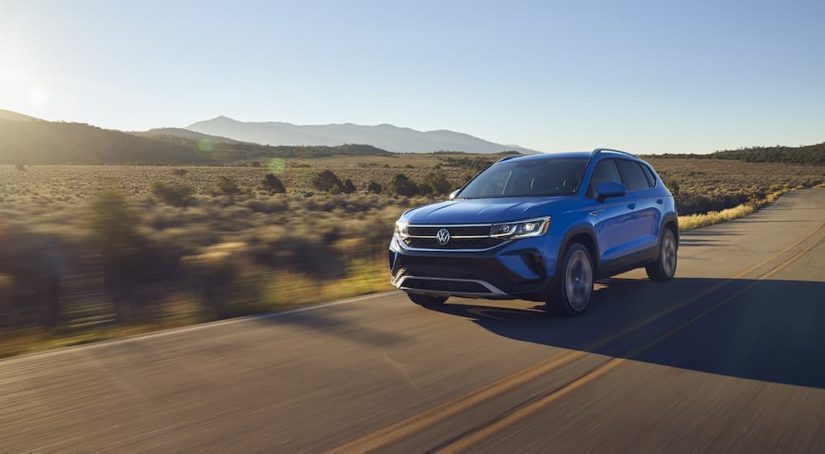 A blue 2022 Volkswagen Taos is shown on an open road after visiting a Volkswagen dealer.
