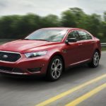 A red 2017 Ford Taurus SHO is shown from the front at an angle while it drives down the road after leaving a Pueblo used car dealer.