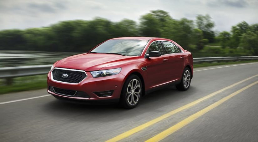 A red 2017 Ford Taurus SHO is shown from the front at an angle while it drives down the road after leaving a Pueblo used car dealer.