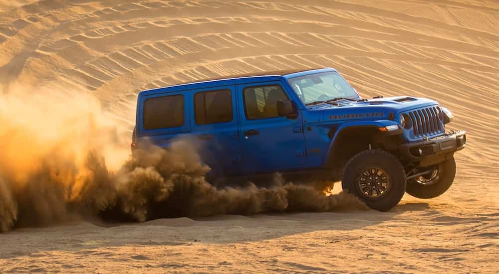 A blue 2021 Jeep Wrangler Rubicon 392 is shown from the front at an angle as it drives over sand dunes after leaving a Colorado Springs Jeep Wrangler dealer.
