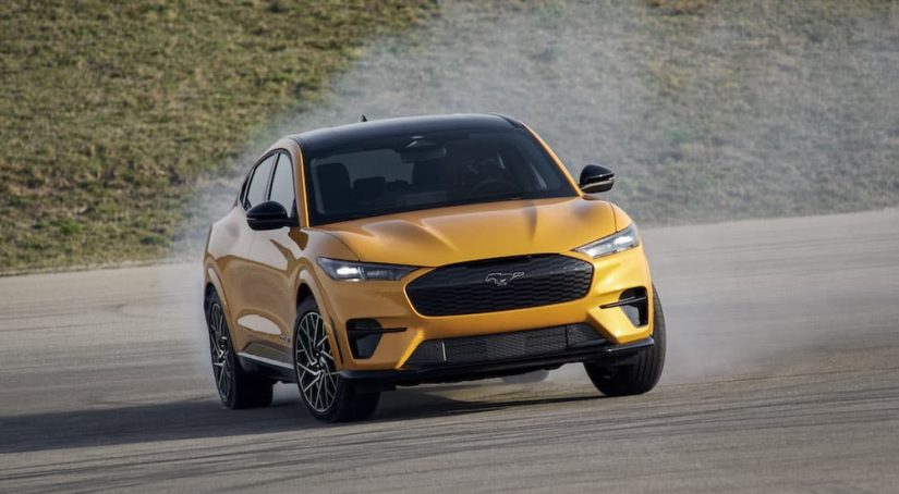 A yellow 2022 Mustang Mach-E GT is shown from the front while sliding on a racetrack after leaving a Fair Oaks Ford dealership
