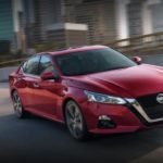 A red 2022 Nissan Altima is shown from the front at an angle while it drives over a bridge during a 2022 Nissan Altima vs 2022 Honda Accord comparison.