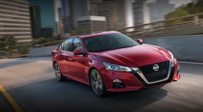 A red 2022 Nissan Altima is shown from the front at an angle while it drives over a bridge during a 2022 Nissan Altima vs 2022 Honda Accord comparison.